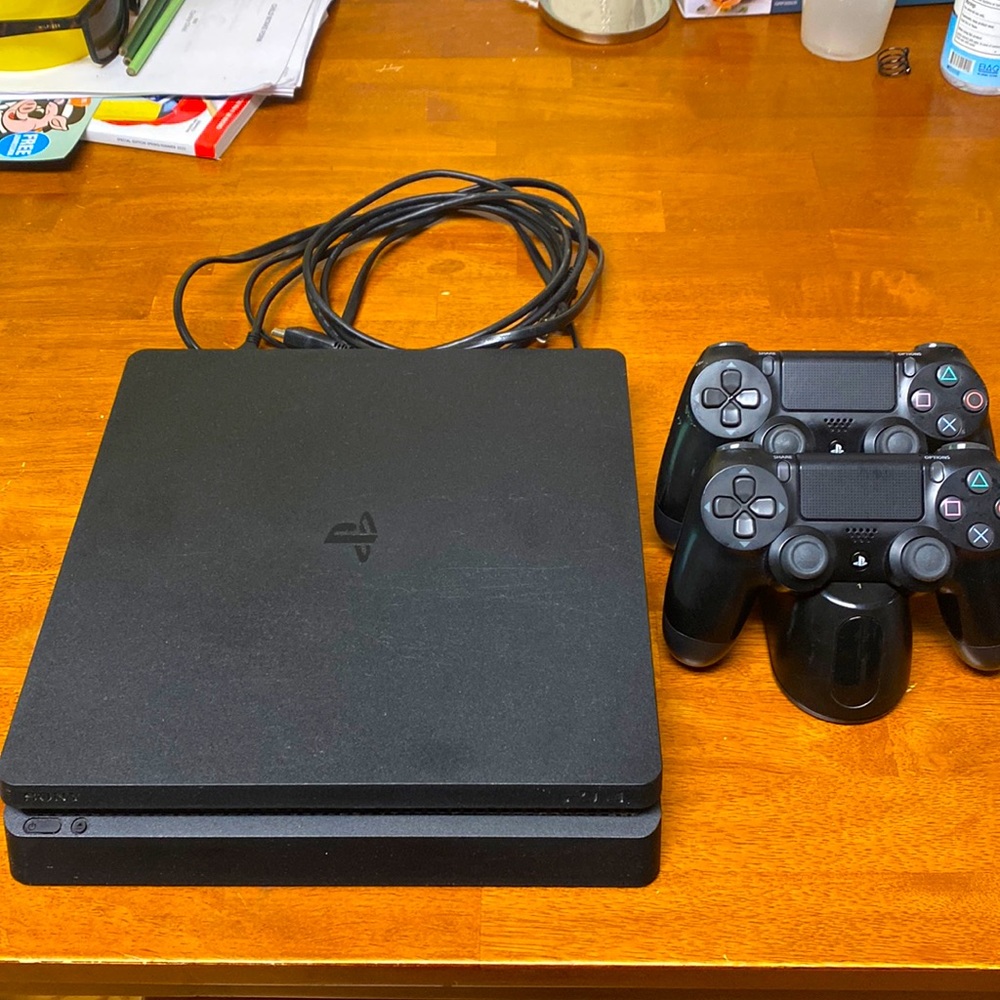 Black PlayStation 4 counsel with 2 controllers and controller charging port